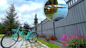 A turquoise bicycle parked on a stone pathway, a wooden fence, and a garden with pink flowers.