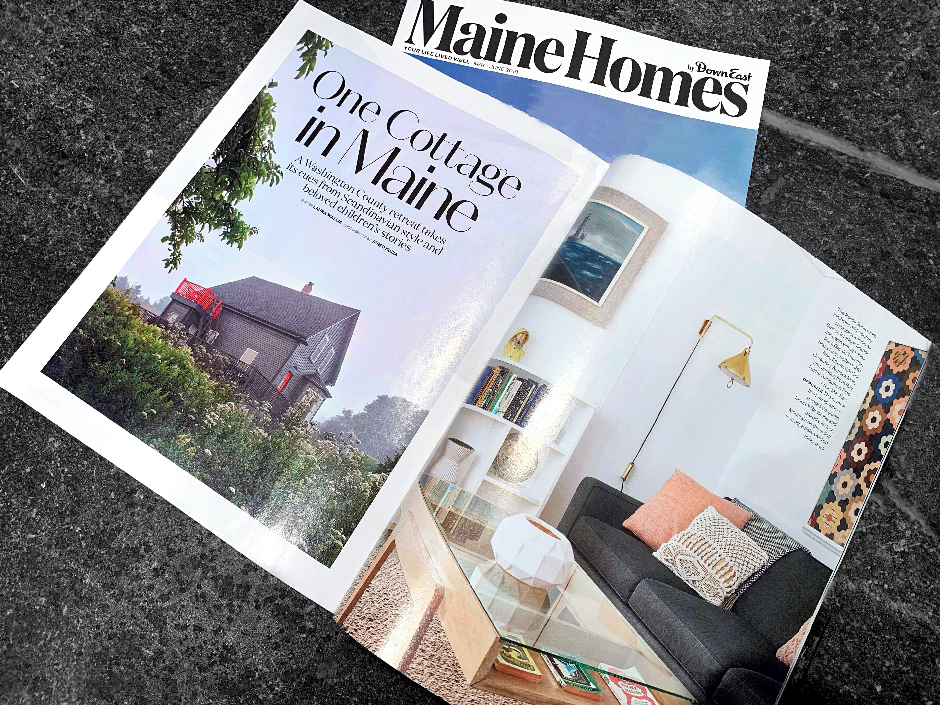 A magazine spread featuring a cottage in Maine with a glass table, a sofa, and a bookshelf.