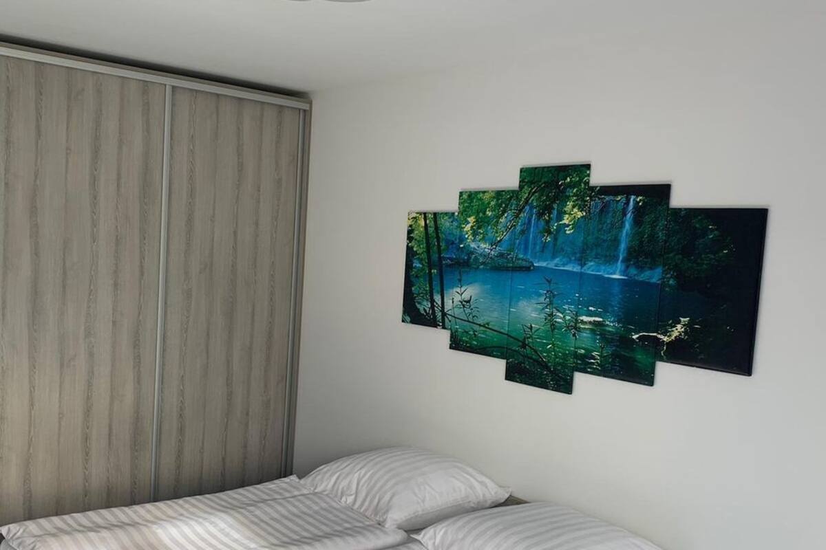 A bedroom with a bed, a wooden wardrobe, and a wall-mounted artwork of a forest scene.