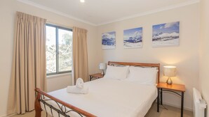 A hotel room with a bed, a nightstand, a lamp, and three framed pictures on the wall. - Boronia - 5/30 Nettin Circuit (Jindabyne)