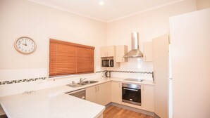 A compact kitchen with a sink, microwave, stove, and a clock on the wall. - Boronia - 5/30 Nettin Circuit (Jindabyne)