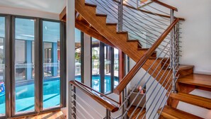 Una escalera moderna con escalones de madera y barandillas metálicas, que conduce a un balcón con vista a una piscina.
