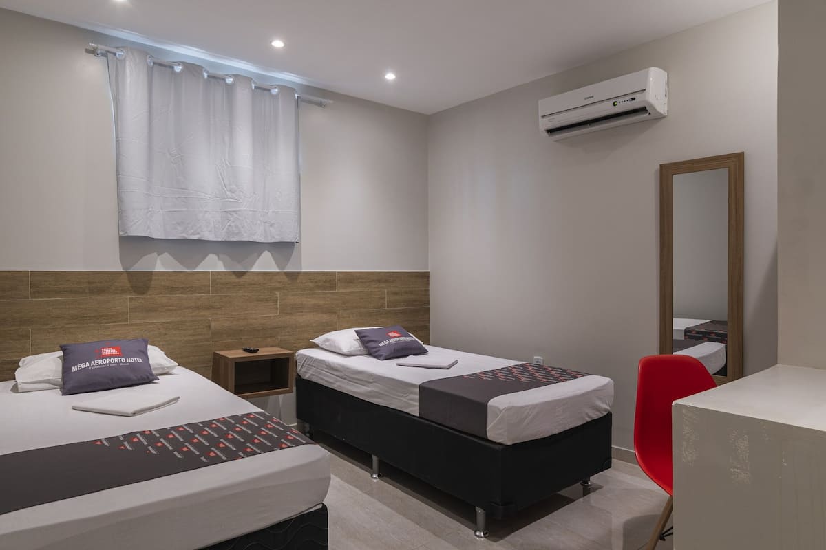 A hotel room with two beds, a red chair, a desk, and a large mirror.