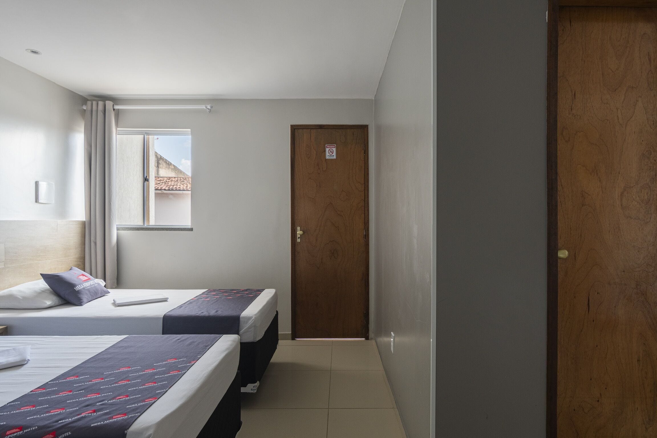 A hotel room with two beds, a window, a door, and a view of the outside.