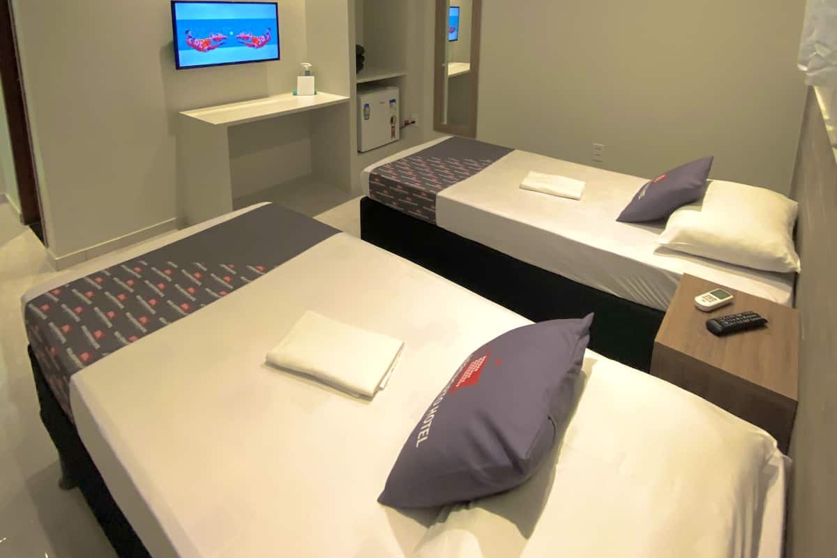 A hotel room with two beds, a TV, a mirror, and an air conditioning unit.