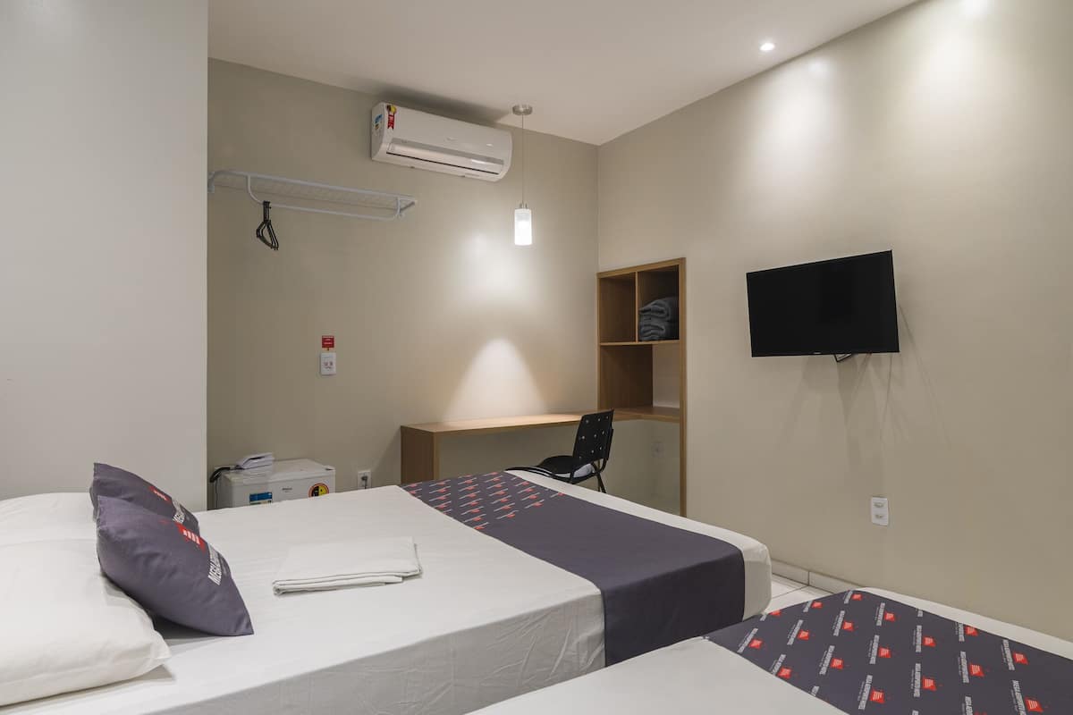 A hotel room with two beds, a desk, a chair, a television, and an air conditioning unit.