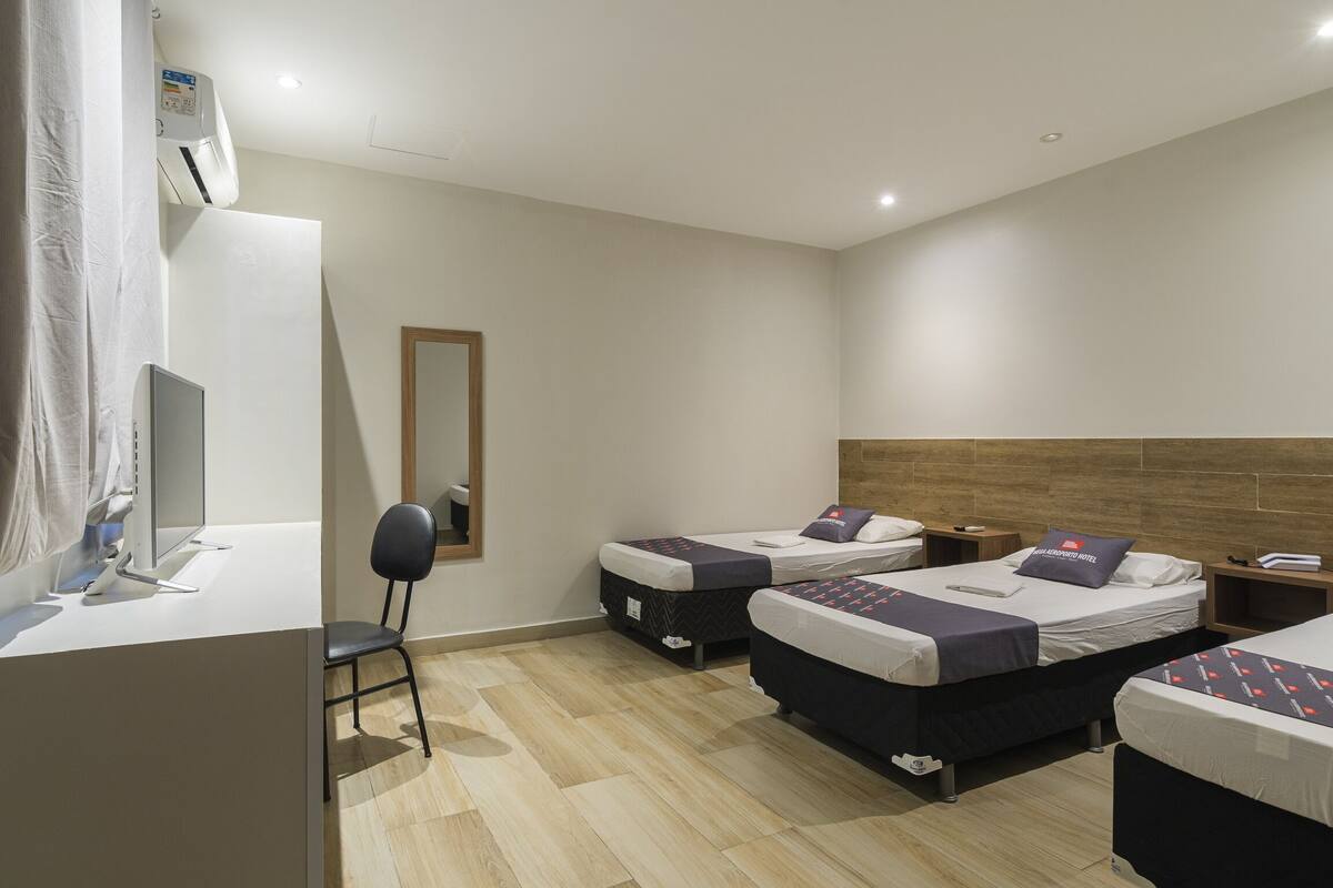 A hotel room with two single beds, a desk with a chair, a mirror, and a wooden headboard.