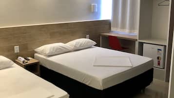 Two single beds with white linens and a wooden headboard, a desk and chair, and a small refrigerator.