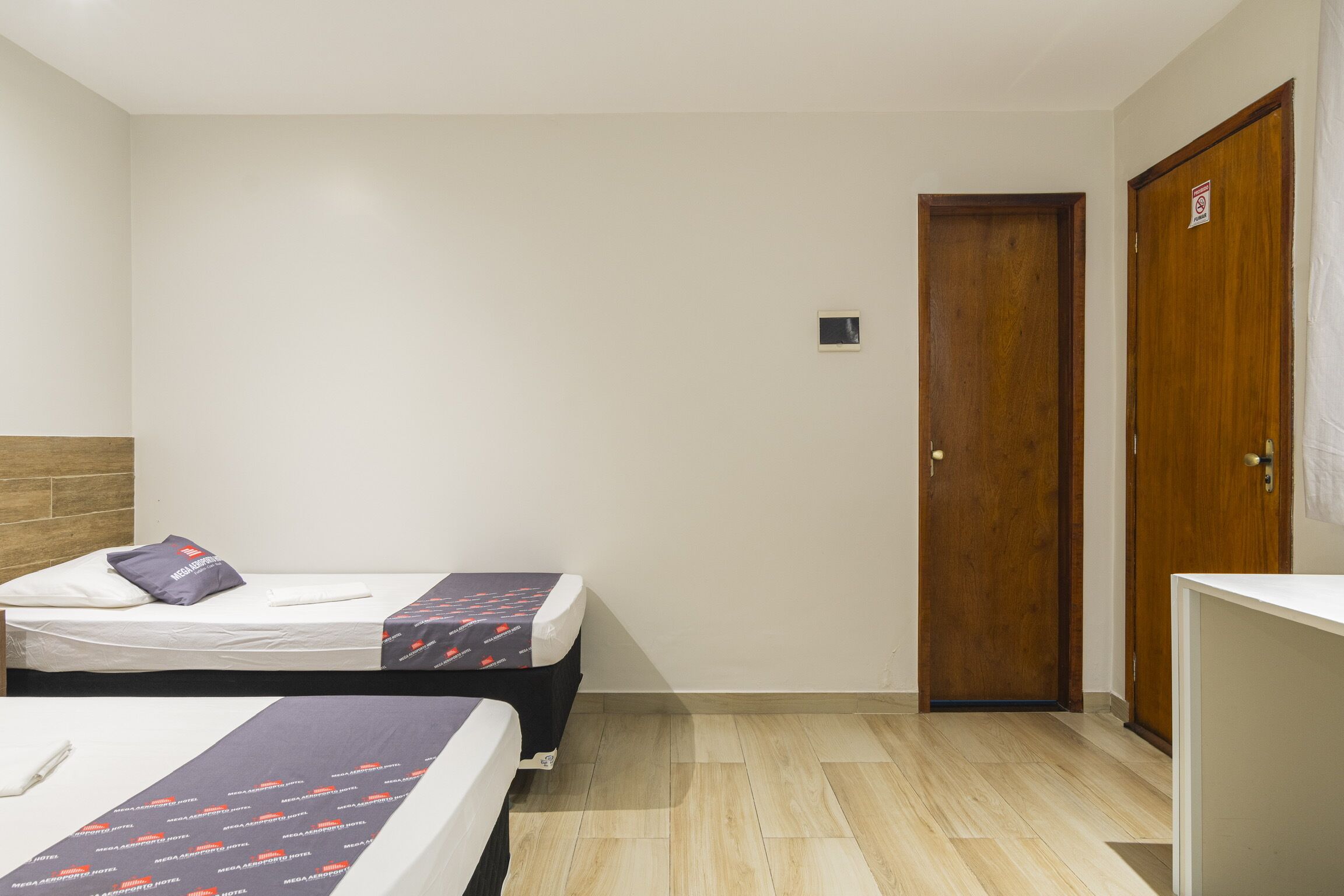 Habitación de hotel con dos camas, una puerta de madera y un ventanal pequeño.