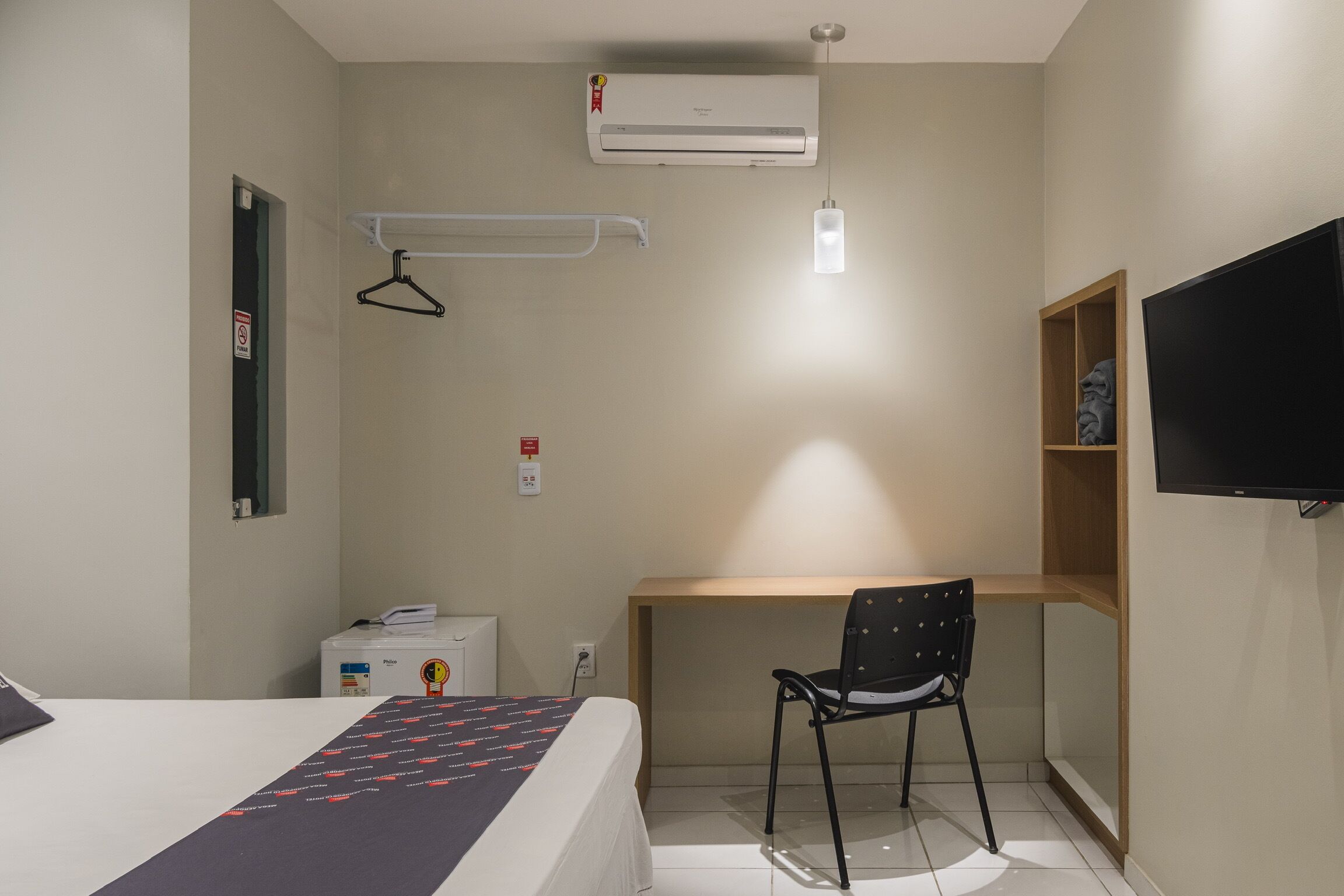 Habitación de hotel con cama, escritorio, silla, televisión, aire acondicionado y una estantería con una estatua.