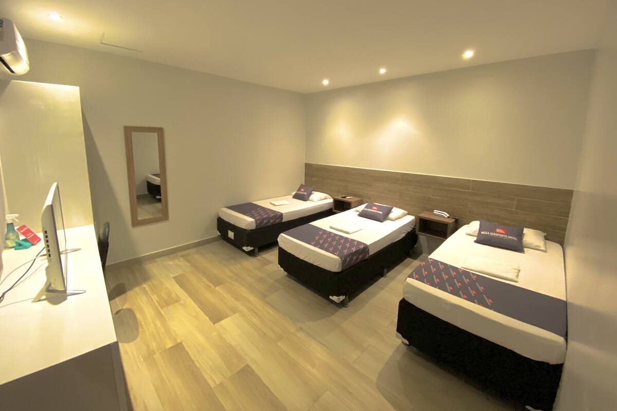A hotel room with three beds, a desk with a computer, and a mirror.