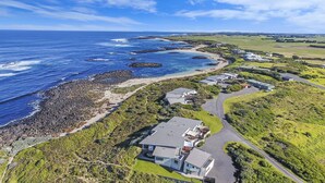 An aerial view of a coastal property with a large house, a beach, and rocky coastline. - Hearns Beachside Villa 3 (Port Fairy)