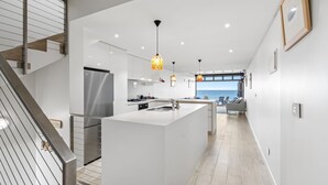 Una cocina moderna con una isla central, electrodomésticos de acero inoxidable, iluminación colgante y vistas al mar.