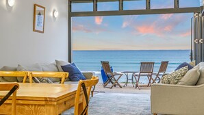 Una habitación con un ventanal grande con vistas al océano, amoblada con un sofá, sillas y una mesa.