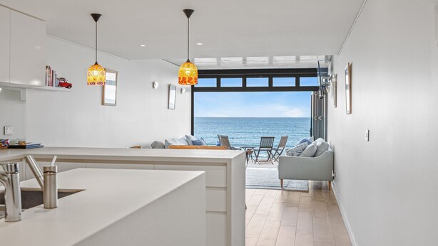 Una cocina moderna con una isla grande, iluminación colgante y vistas al mar a través de un ventanal.