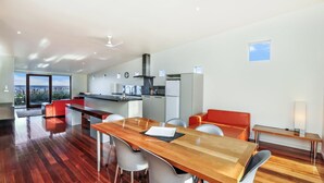 A modern kitchen with a dining area, a view of the ocean, and a small window. - Hearns Beachside Villa 4 (Port Fairy)