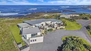 A coastal residential area with modern houses, a paved driveway, and a rocky shoreline. - Hearns Beachside Villa 4 (Port Fairy)