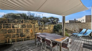 An outdoor patio with a wooden table and chairs, a stone wall, and a covered area with a canopy. - Hearns Beachside Villa 4 (Port Fairy)