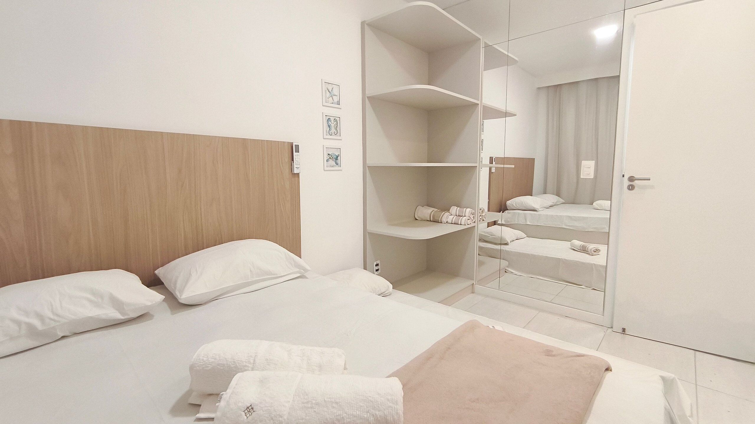 Una habitación de hotel con cabecera de madera, cama con ropa blanca, armario con repisas y un espejo.
