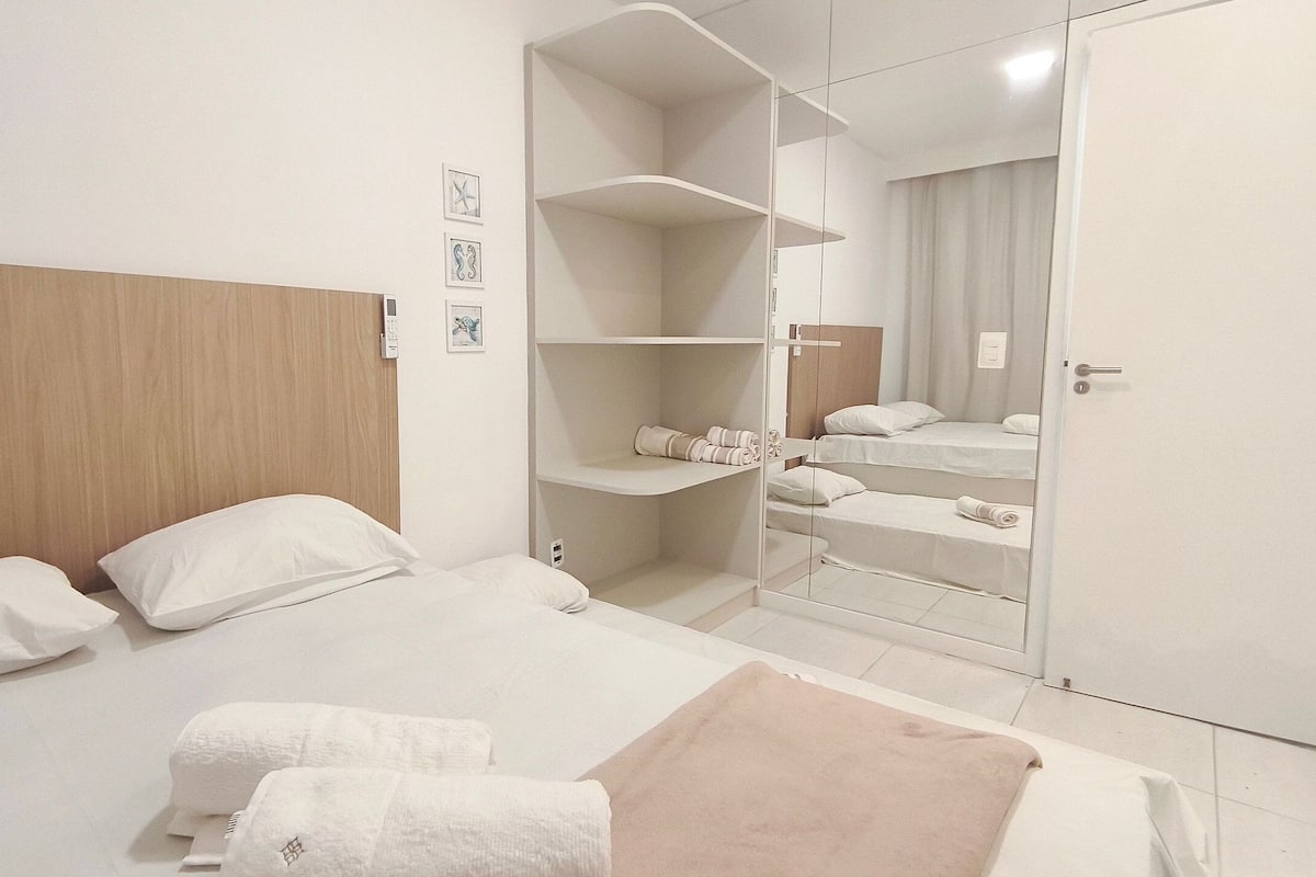 A hotel room with a wooden headboard, a bed with white linens, a closet with shelves, and a mirror.