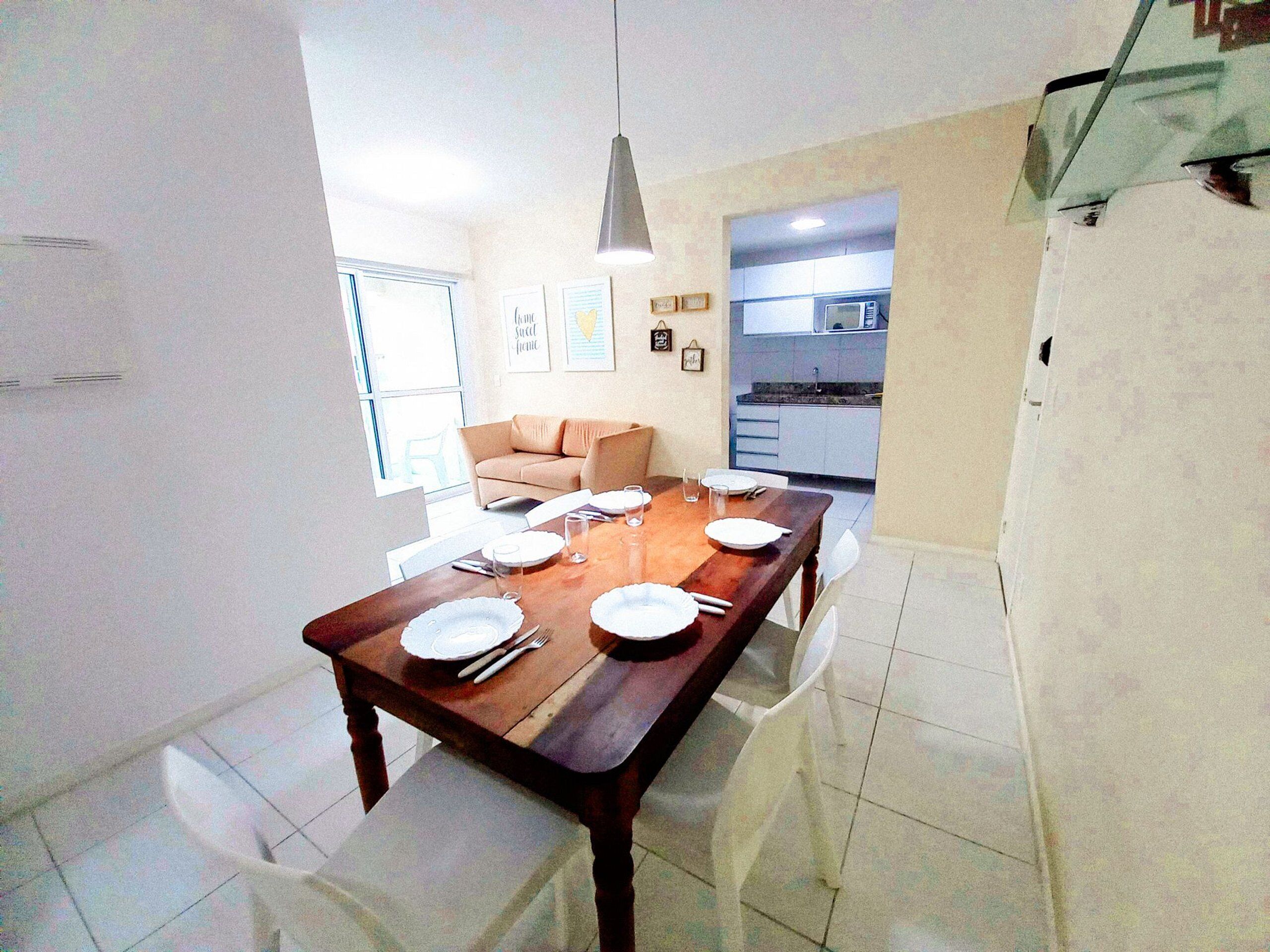 A dining area with a wooden table set for four, white chairs, and a kitchen in the background.