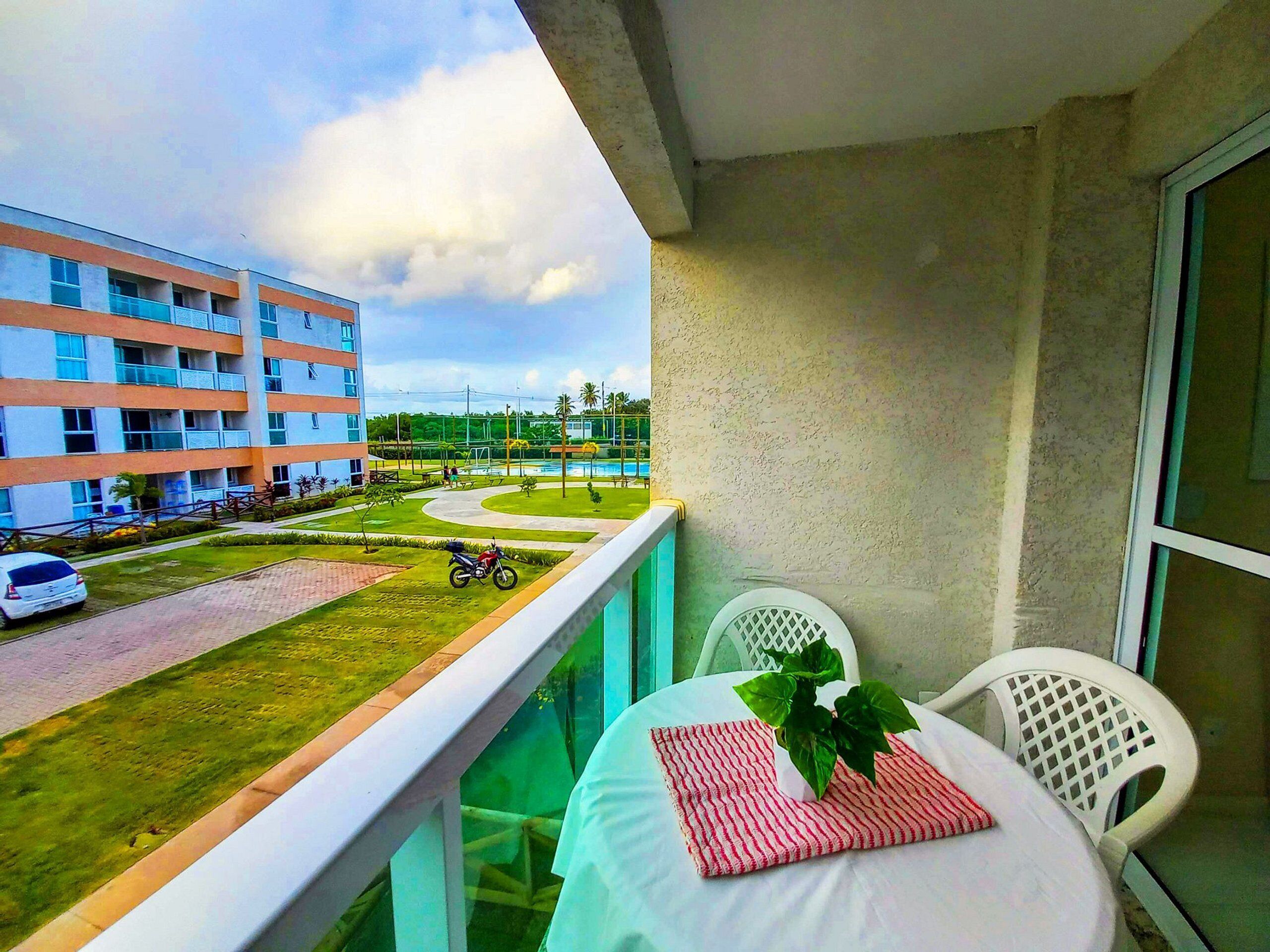 A balcony with a view of a building, a swimming pool, and a parked motorcycle.