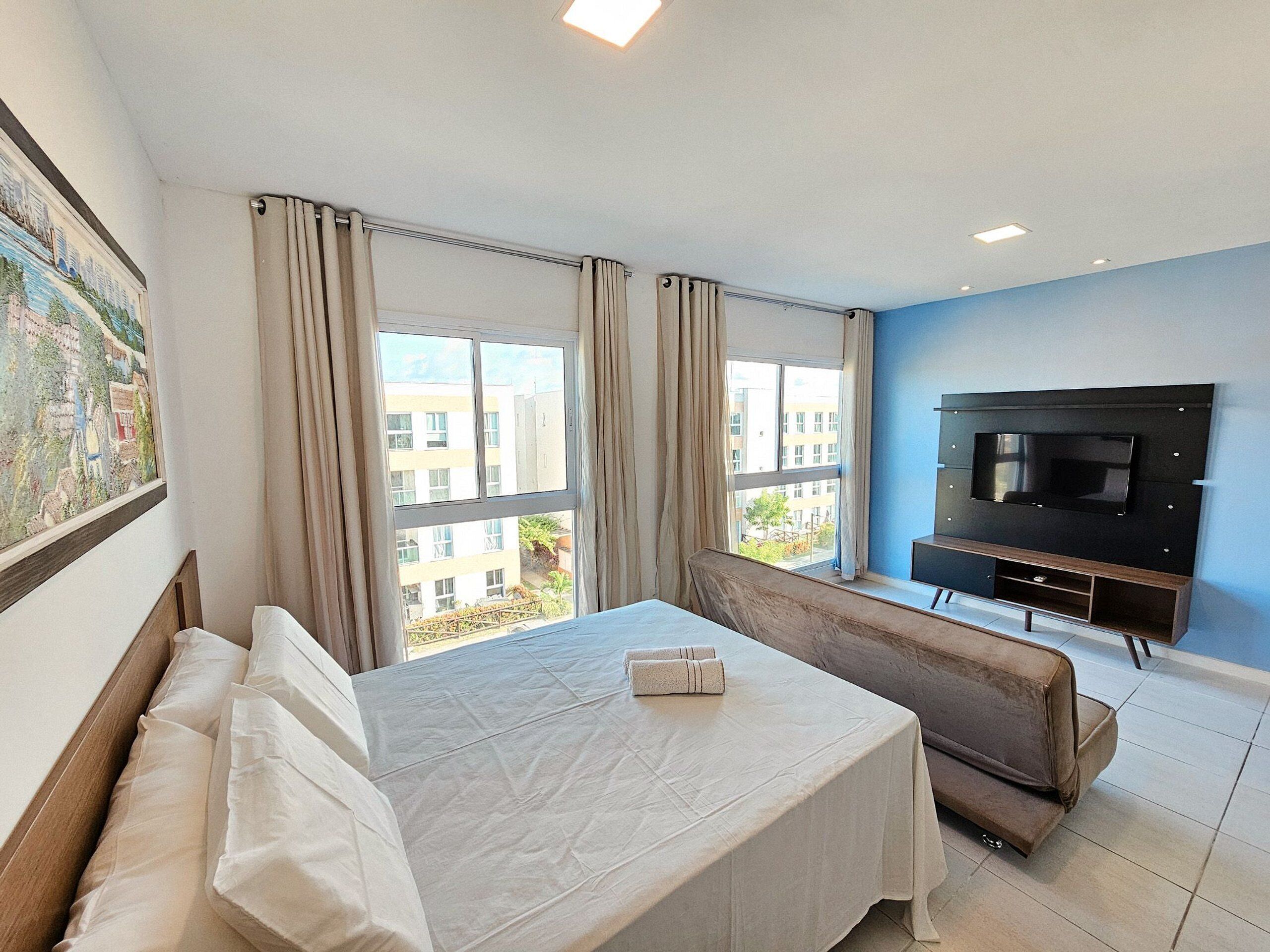 Una habitación de hotel con cama, sofá, televisión y ventanas amplias.