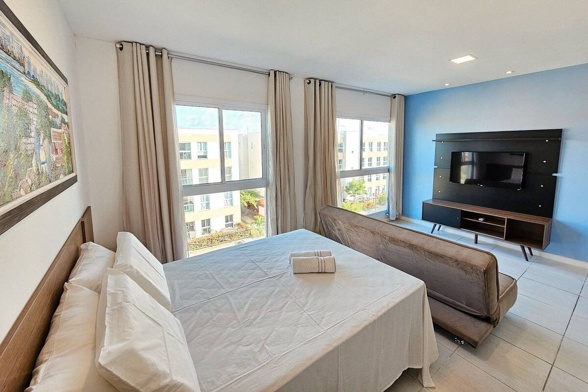 Una habitación de hotel con cama, sofá, televisión y ventanas amplias.