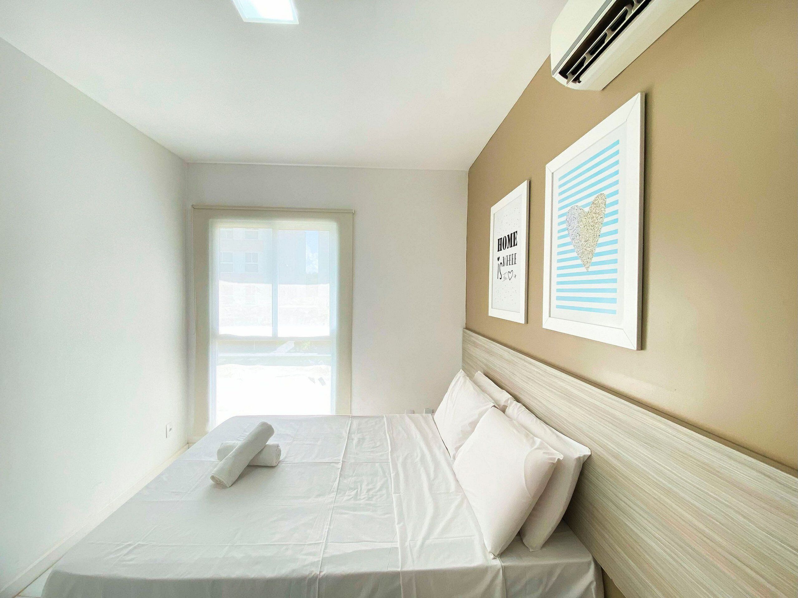 A hotel room with a bed, a window, and two framed pictures on the wall.