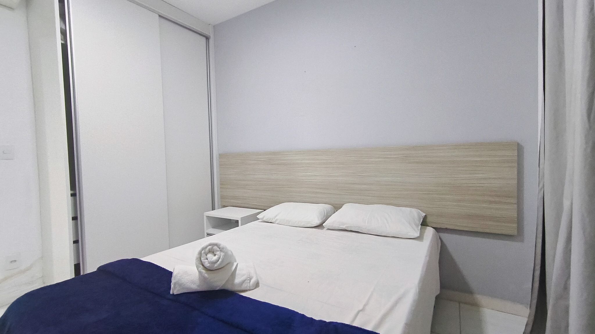 A hotel room with a bed, a nightstand, and a wooden headboard.