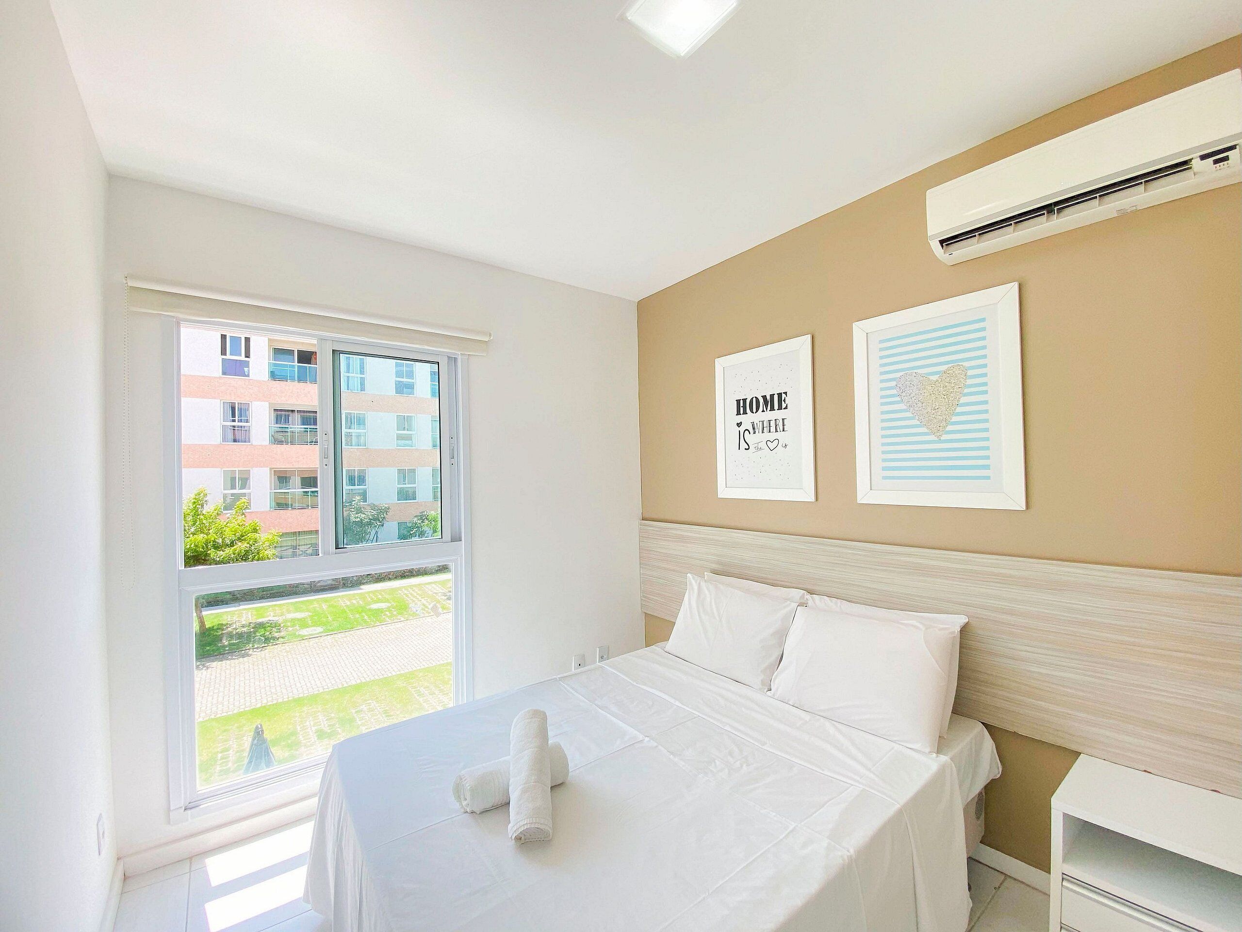 Una habitación de hotel con cama, ventana con vista a edificios y dos cuadros en la pared.