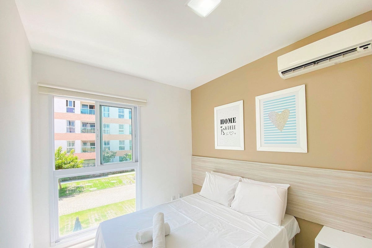 Una habitación de hotel con cama, ventana con vista a edificios y dos cuadros en la pared.