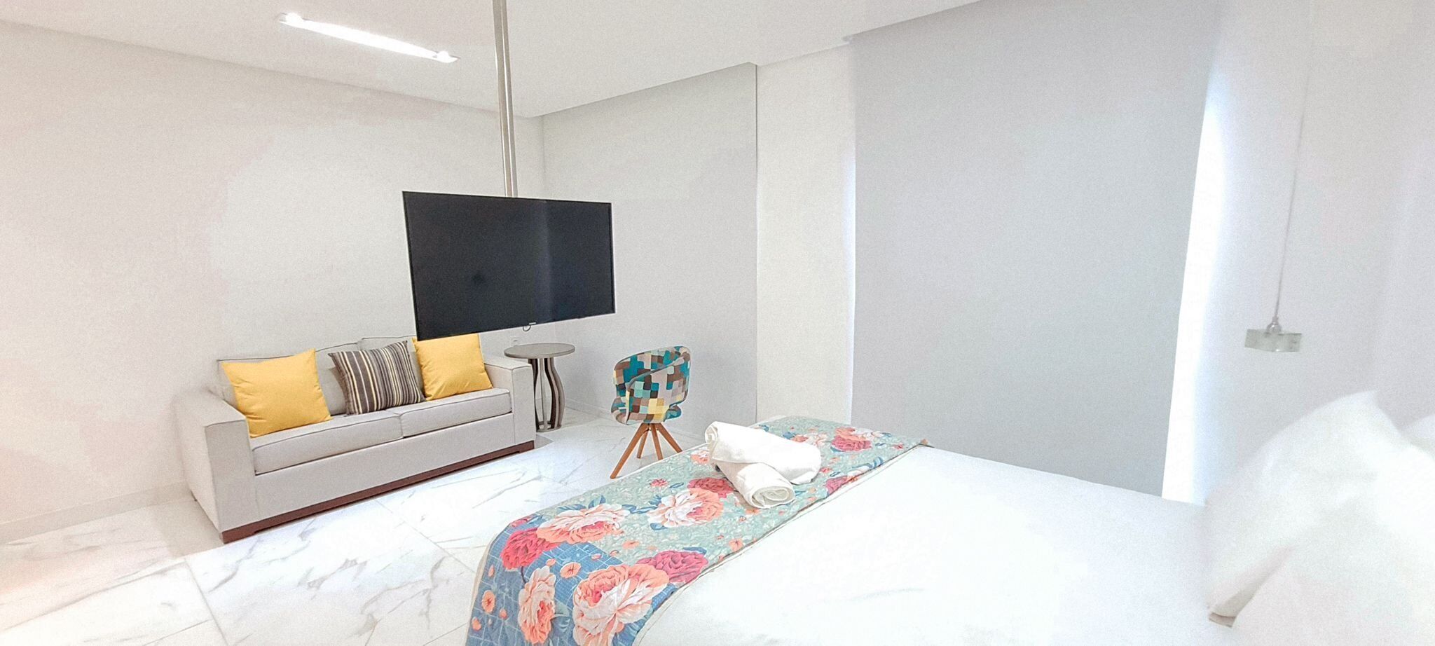 A modern bedroom with a bed, a sofa, a TV, and a small table.