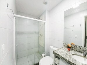 Un baño con cabina de ducha de vidrio, inodoro, lavabo con encimera de granito y espejo.