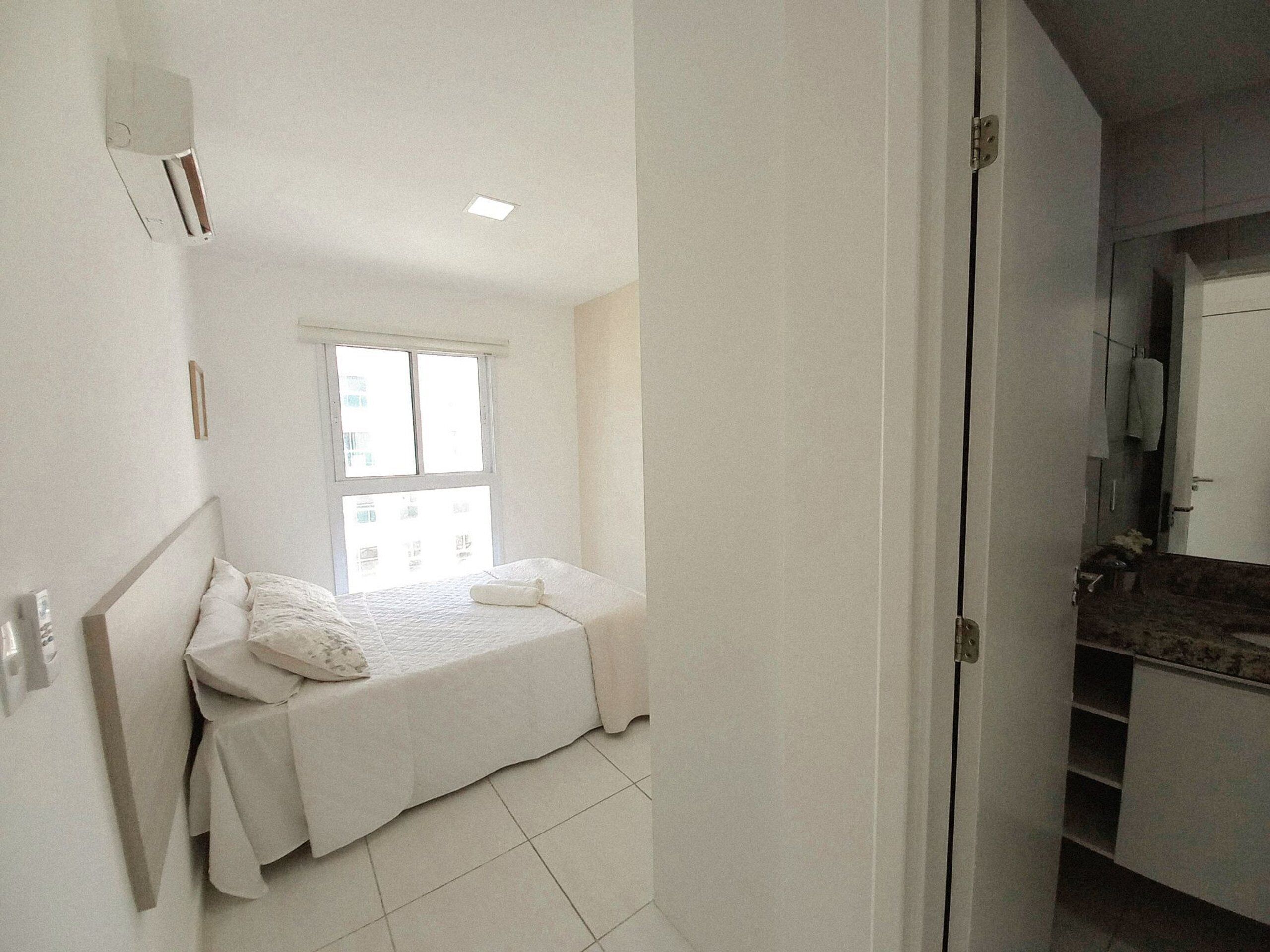 A small, bright bedroom with a single bed, a window, and a bathroom visible through an open door.