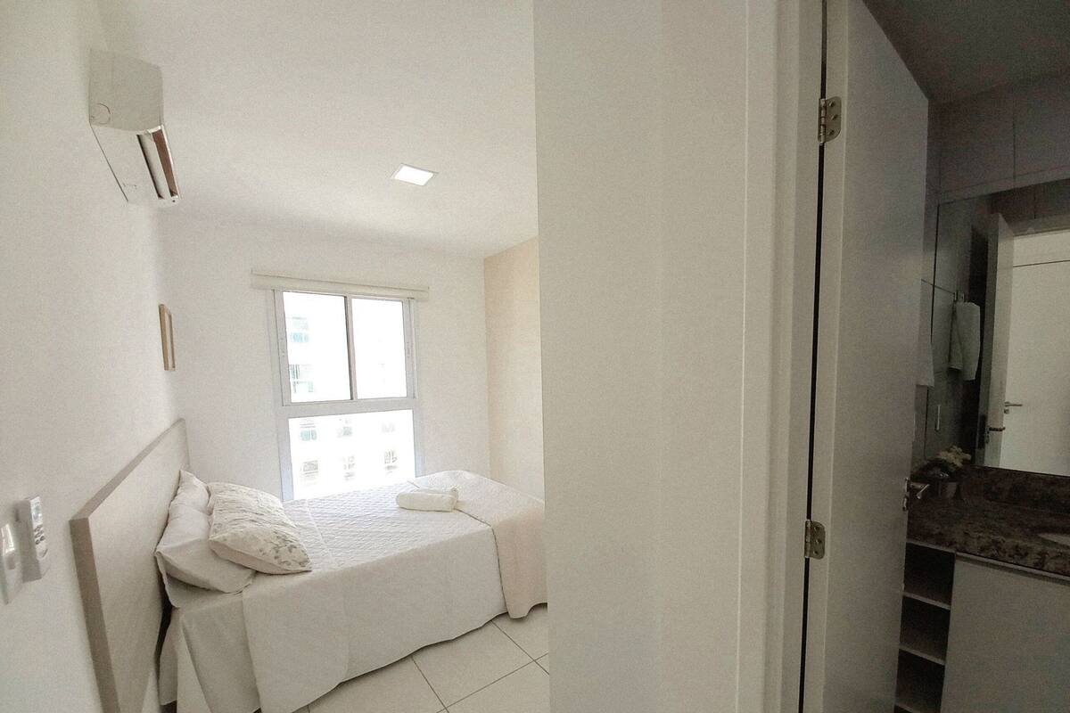 A small, bright bedroom with a single bed, a window, and a bathroom visible through an open door.