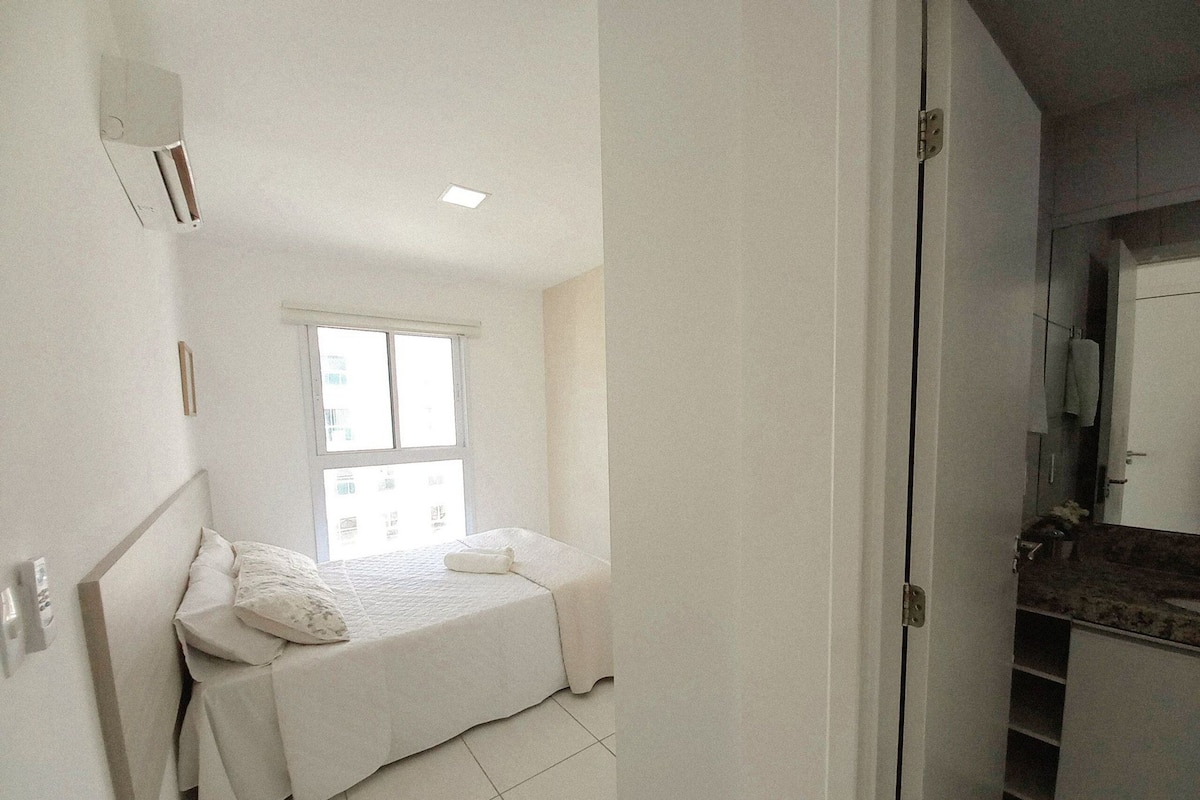 A small, bright bedroom with a single bed, a window, and a bathroom visible through an open door.