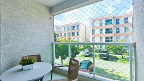 Un balcón con una mesa blanca y dos sillas, con vista a un estacionamiento y un edificio con varias ventanas.