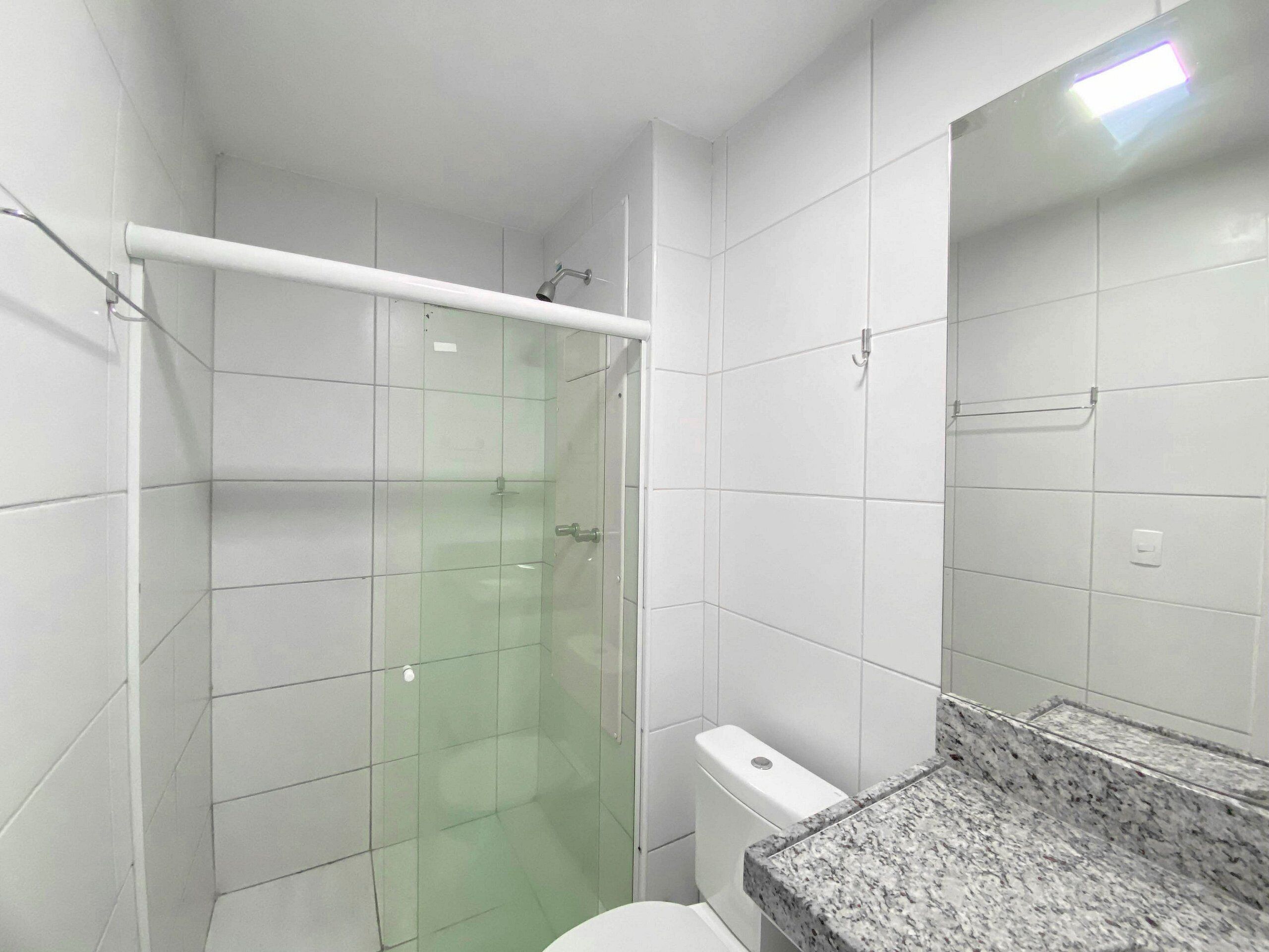 A bathroom with white tiled walls, a glass shower enclosure, a white toilet, and a granite countertop.
