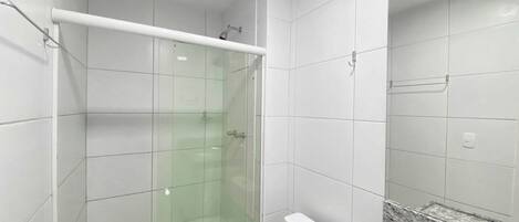 A bathroom with white tiled walls, a glass shower enclosure, a white toilet, and a granite countertop.