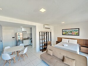 A modern, well-lit room with a kitchenette, a dining area with a table and chairs, a sofa, and a bed with a headboard. - Flats no Muro Alto Club (Ipojuca)