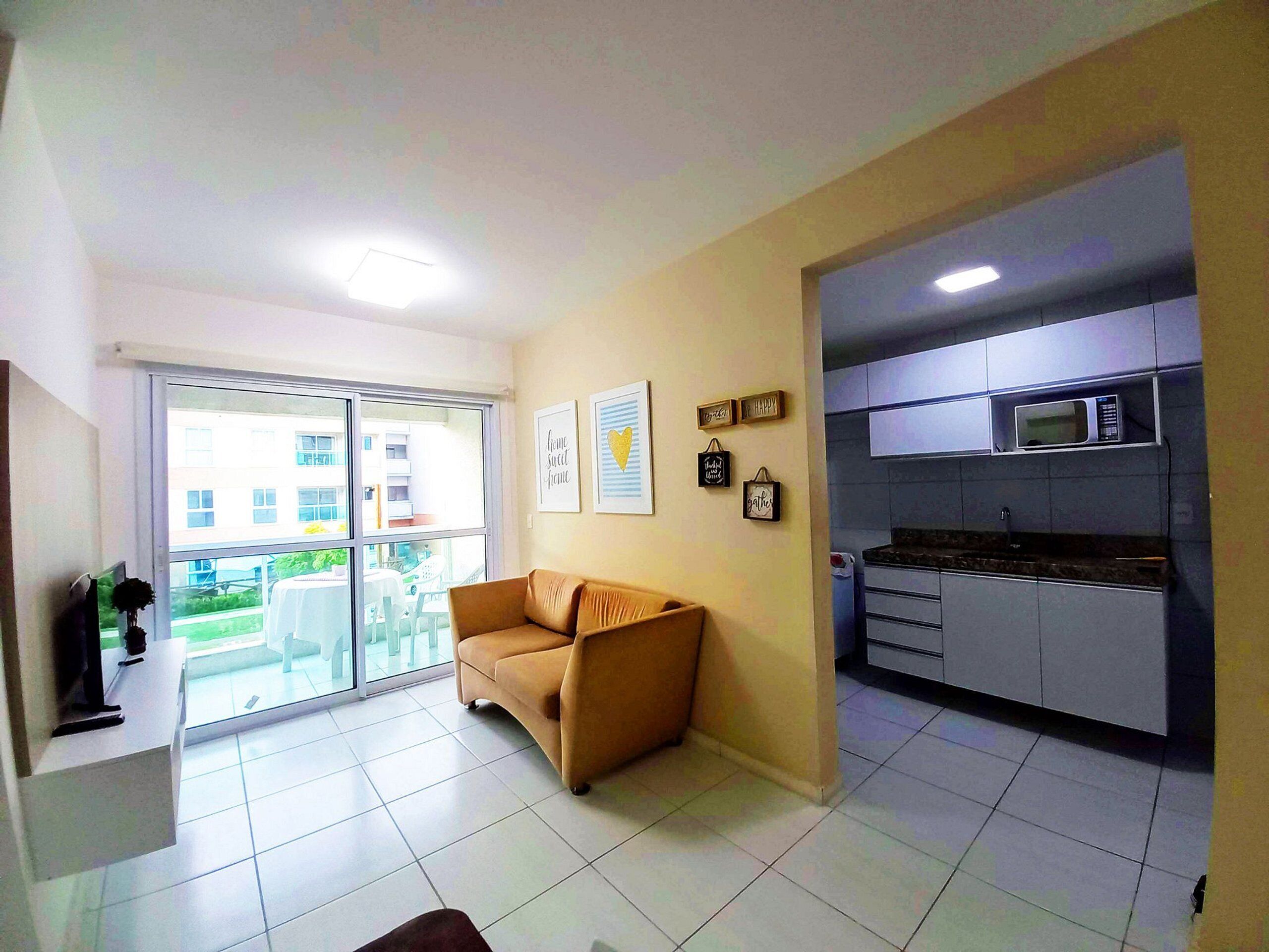 A living room with a sofa, a kitchen with modern appliances, and a balcony with a view of buildings.