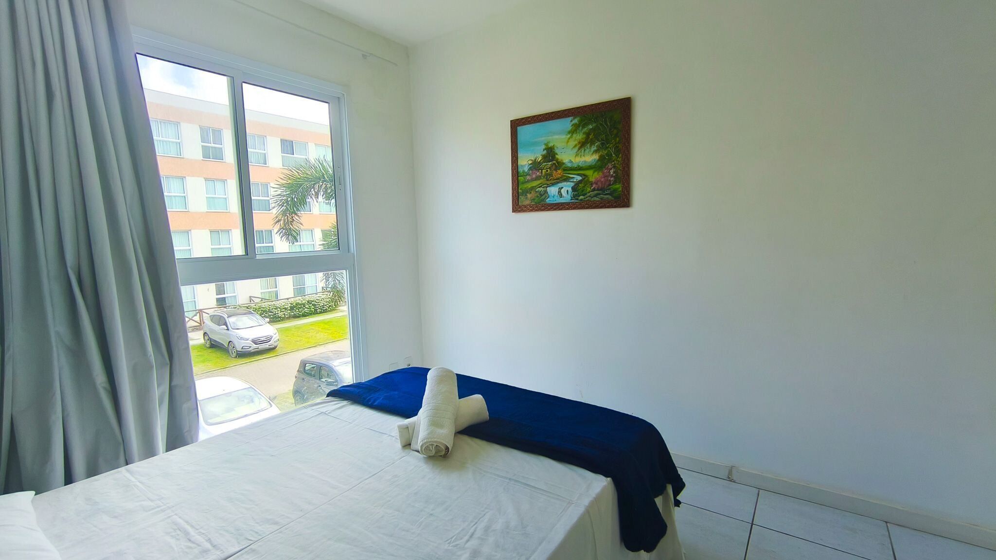 Una habitación de hotel con una cama, un ventanal con cortinas y un cuadro en la pared.