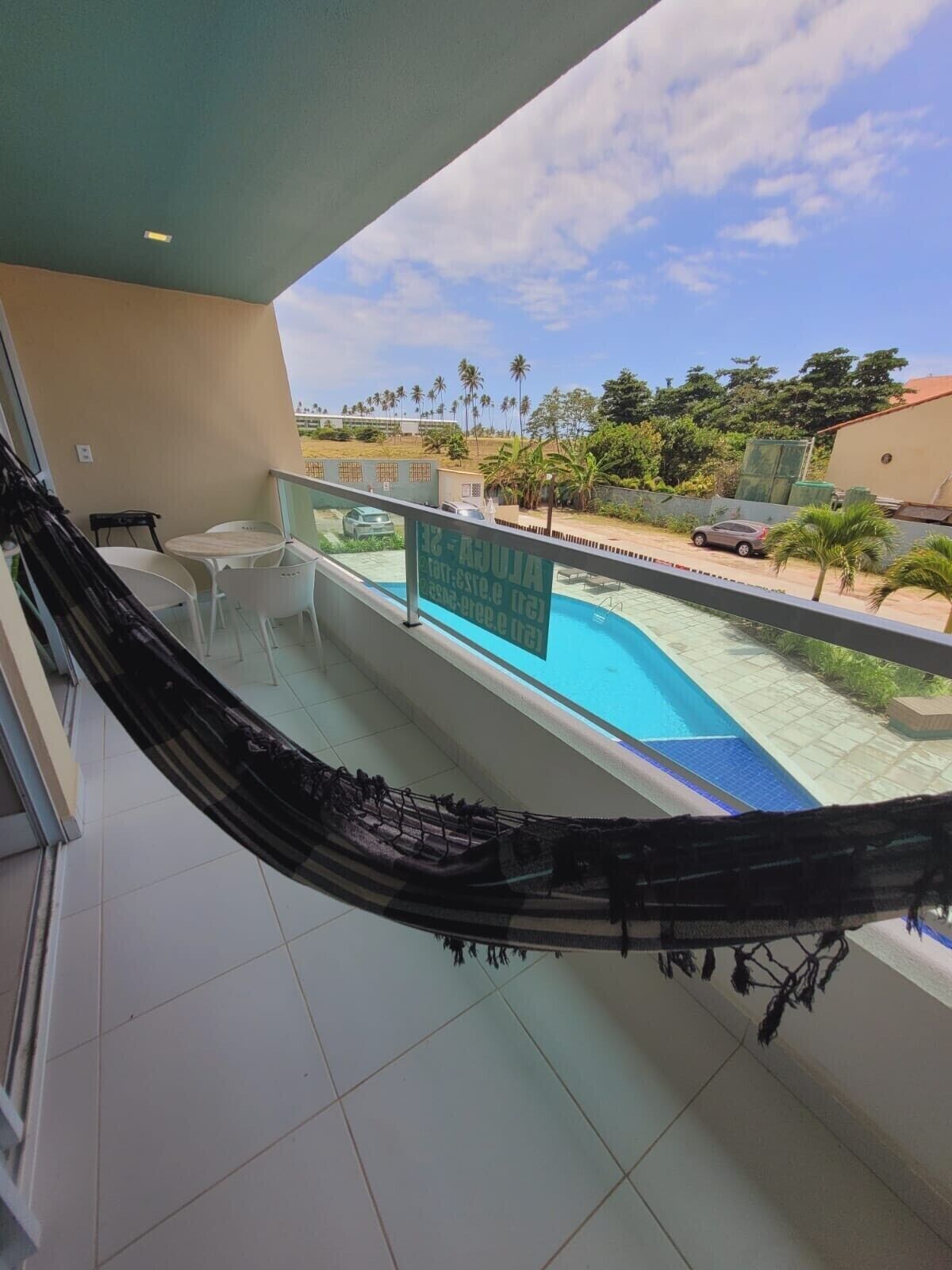 A balcony with a hammock, a pool, and a view of palm trees and a road.
