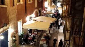 A narrow street with outdoor seating and people walking. - Marconi Rooms - Loggia delle Erbe (Verona)