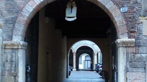 An arched stone gateway with a bell, leading to a street with parked cars and a building with a number plaque. - Marconi Rooms - Loggia delle Erbe (Verona)