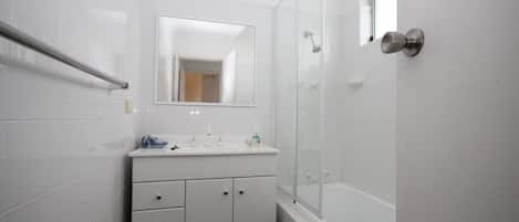 Un baño moderno con cabina de ducha de vidrio, tocador blanco con espejo y barra de apoyo.