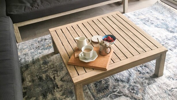 Ein Holztisch mit einer Ablage, auf der zwei Kaffeetassen, ein Teekessel und eine Obstschale stehen.