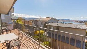 Un balcón con una parrilla, mobiliario exterior y vistas a un lago y montañas.