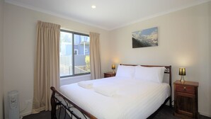 Una cama bien hecha en una habitación de hotel, con un gran ventanal, un cuadro en la pared y lámparas de noche.